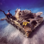 Scuba diver exploring a sunken tank wreckage on the ocean floor. - CertiDive